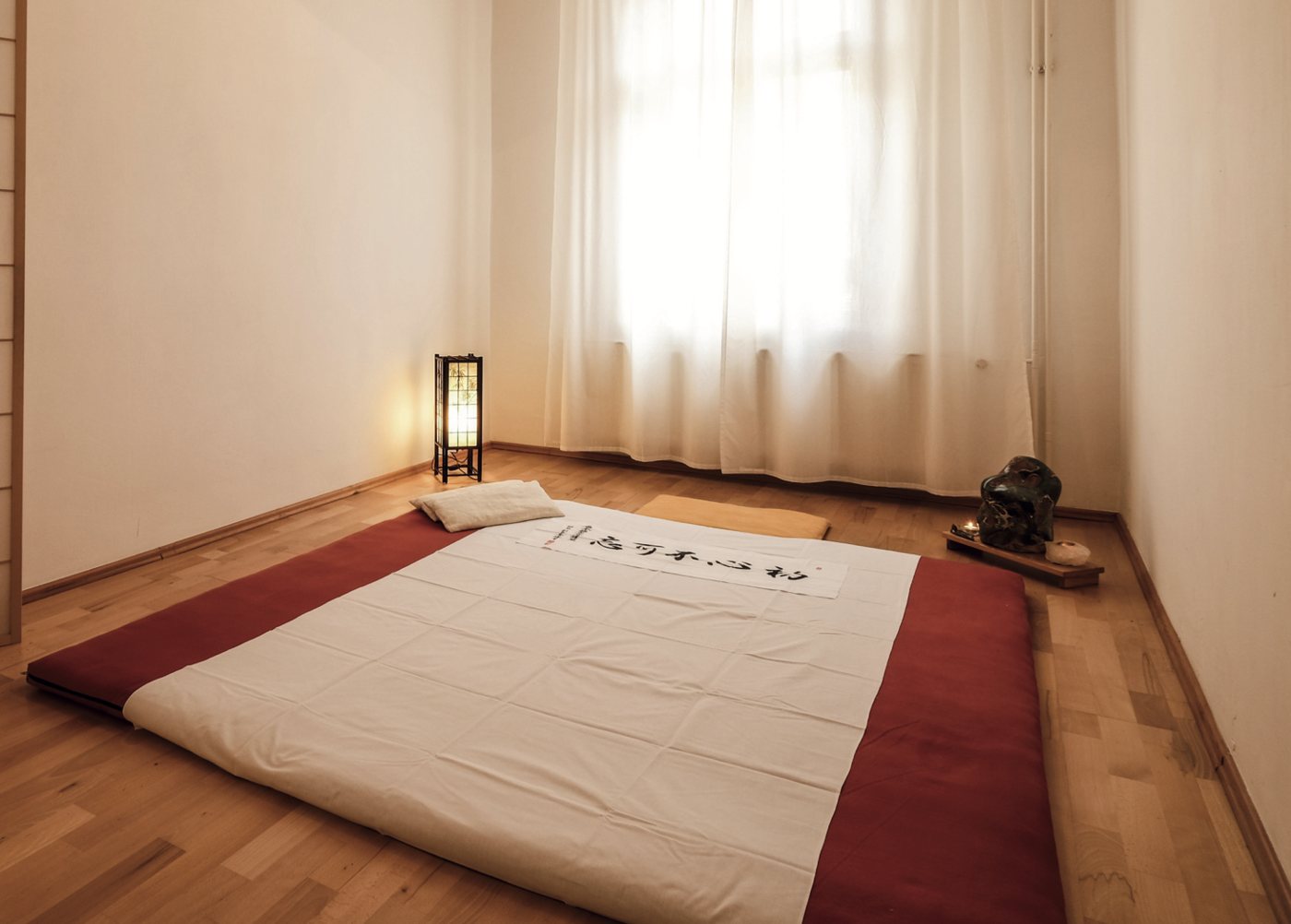 Behandlungsraum in Berlin: Shiatsu-Matte am Boden, helles Fenster mit Vorhang, Lampe und Kerze